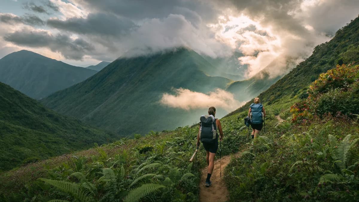 Two hikers with trekking poles advancing on a scenic mountain trail through cloud forest and Andean mountain ridges in Antioquia