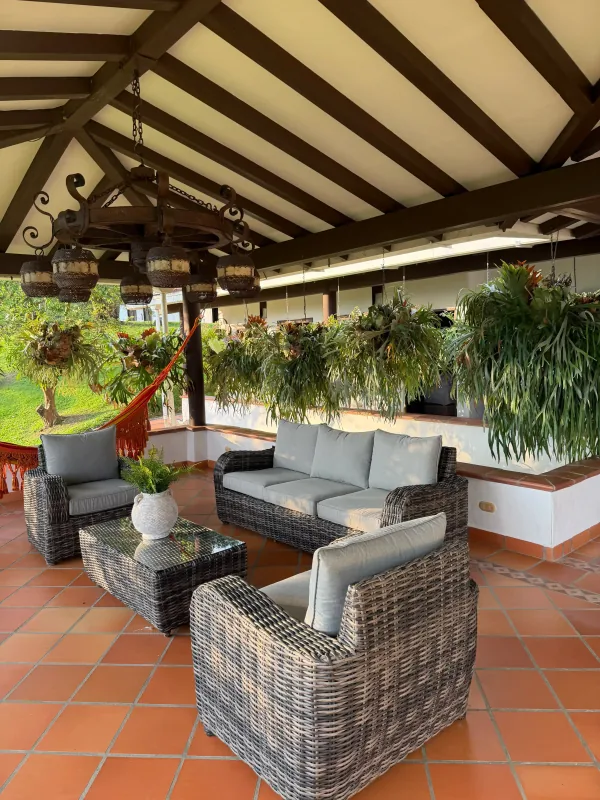 Open-air covered lounge at La Juana with wicker armchairs, hammock, and hanging ferns
